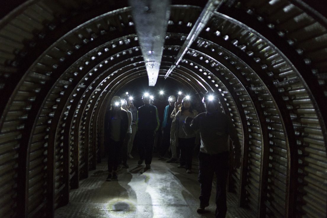 A deep long tunnel, illuminated with group of people wearing helmets with torches.